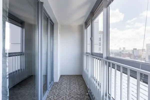 Przykładowe wnętrze balkonu w bloku, idealne do rozważenia, jak zabudować balkon w bloku, z przeszklonymi drzwiami i oknami wychodzącymi na miasto.